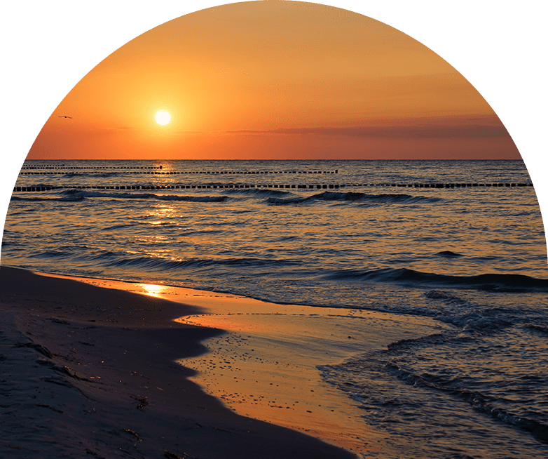 Sunset over a calm ocean with waves gently hitting the shore.